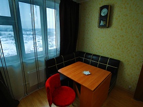 деревянные часы с маятником на стене над черным с белой полоской уголком,белая с черной полоской гардина и темные шторы на окне кухни с белой мебелью трехкомнатной квартиры в переезде