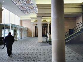 светлая плитка на полу престижного подъезда элитного современного дома с лифтами, экскалатором и стеклянным коридором на первом этаже