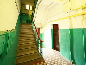 лестница с перилами в подъезде немецкой трехэтажки с почтовыми ящиками на стене с зелеными панелями