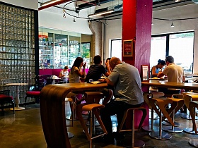 деревянные барные стойки и стулья вокруг красной колоны, столы у больших окон кафе на территории Бизнес центра в стиле лофт