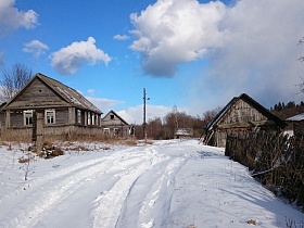 сугробы снега на улице заброшенной деревни со старыми деревянными домами