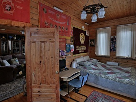 открытая дверь в спальню с многочисленными флагами на стене над кроватью и компьютерным столом  современной деревянной загородной дачи