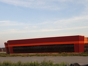 просторное симпатичное здание кирпичного цвета с красной отделочной полосой над панорамными окнами торгового центра вдоль дороги в Учинском районе