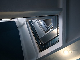  редкая бетонная винтовая лестница с серыми металлическими перилами и деревянными поручнями в подъезде жилого девяти этажного дома с площадки на первом этаже