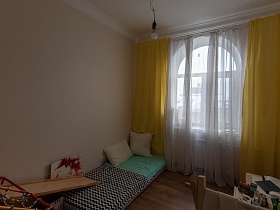 ранний старт, кровать с белыми подушками у окна с желтыми шторами и белой гардиной на арочном окне детской комнаты