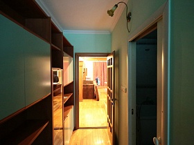 открытая дверь в ванную комнату из длинного коридора с коричневым шкафом с открытыми полками у голубой стены современной двухкомнатной квартиры