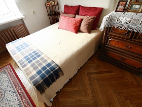 красные и бежевые подушки на белом покрывале большой кровати в спальной комнате сталинки