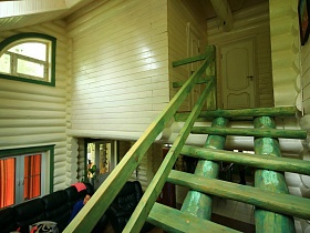 зеленая деревянная лестница с перилами из двух бревен на второй этаж светлой комнаты темной дачи-сруб директора
