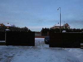 широкие коричневые ворота коричневого забора коттеджных двухэтажных домиков из кирпича нейтрального цвета