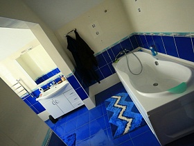 белая ванна и зеркало над раковиной в тумбе в ванной комнате с синей плиткой на полу и стене современного кирпичного дома