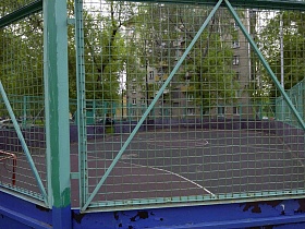 спортивная площадка за высоким забором с металлической сеткой в коммунальном дворе