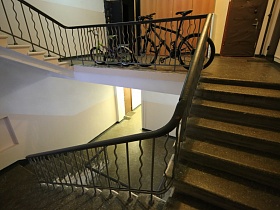 детский салатовый велосипед и черный взрослый у металлических перил лестницы на бетонной площадке этажа 9 подъезда на Красноказарменной