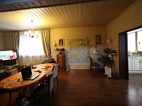 белая люстра над большим столом с ноутбуком и стульями вокруг, картины и карта на светлой стене гостиной в современном деревянном трехэтажном доме
