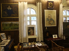 икона, портреты и картины на стене между окнами с белыми шторами в комнате советской художественной деревянной дачи-музей времен СССР