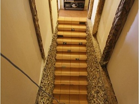 вид сверху на узкий коридор с деревянной лестницей между этажами сказочного дома с интересным обрамлением панелей и деревянной отделкой на светлых стенах