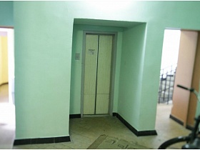 голубые стены площадки у дверей лифта с выходом на лестничную площадку и общий коридор с квартирами на этаже жилого дома