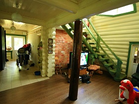 сушилка для белья, детская коляска и темный шкаф в светлой части деревянной дачи и зеленая деревянная лестница на второй этаж