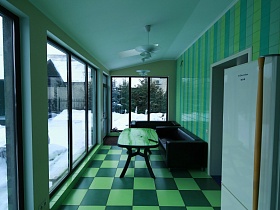 черные кожаные диваны вокруг овального зеленого стола в застекленной яркой кухне с панорамными окнами