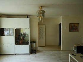 белый шкаф с витриной под стеклом у стены белой гостиной съемной квартиры