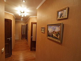 картины и фотографии в рамках на светло-коричневых стенах длиного коридора трехкомнатной квартиры государственного служащего
