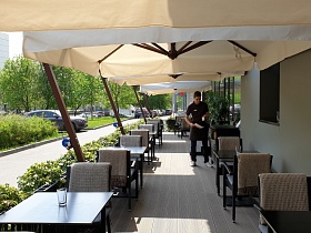 ровные ряды столиков на открытой площадке под большими зонтиками с невысоким зеленым живым заборчиком кафе-пиццерии при ресторане