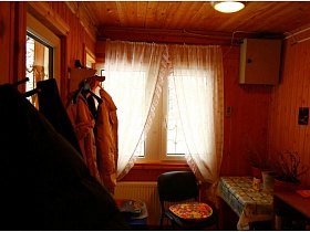 настенная вешалка с одеждой у открытой двери в деревянную прихожую дачи