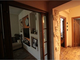 картина в рамке и разнообразные сувениры на полках белой стенки из гипсокартона гостиной через открытую раздвижную дверь