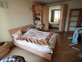 бежевые комод, большая кровать, большой угловой шкаф в спальне с бежевым линолеумом на полу  трехкомнатной квартиры высотного дома