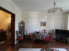 этажерка с книгами, фотографиями и большой плоский телевизор в углах светлой гостиной квартиры педагоа