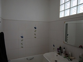 зашитая белая ванна, зеркало над белой столешницей с раковиной и стиральной машинкой под ней в светлой ваной комнате современной квартиры совмещеной с советской