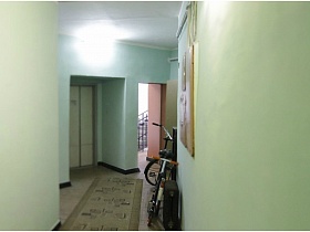 взрослый велосипед у стены коридора с дорожкой на полу у дверей лифта в жилом доме