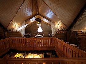 большая люстра, стилизованная под свечи под желтым абажуром на металлических цепях в центре треугольной крыши в проеме с деревянными перилами