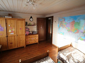 разнообразные наклейки на шкафу для одежды, на комоде и большая карта мира на стене детской спальни в просторном современном деревянном доме