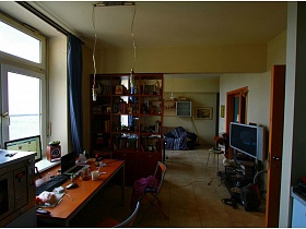 жаровочный шкаф, монитор на подоконнике, ноутбук с клавиатурой на захламленном столе в кухне зонированной комнаты двухкомнатной квартиры с видом на Москва-сити