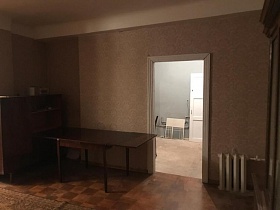 раздвижной коричневый полированный стол, и коричневый сервант у бежевых стен гостиной с линолеумом с квадратами и белым потолком