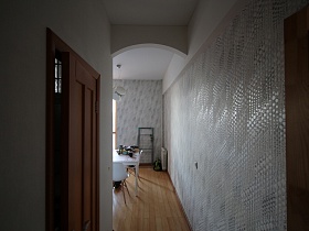 белый обеденный стол со стульями на светлой кухне из коридора с арочным дверным проемом и серыми тесненными обоями на стене квартиры двух эпох в одном помещении