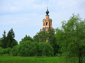 общий вид церкви на горе среди густой зелени лиственных деревьев в живописном месте Подмосковья в летнее время