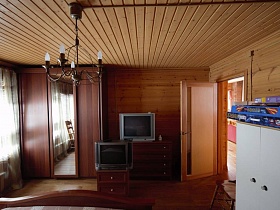 высокий шкаф для одежды с зеркалом посередине и два телевизора на комодах в спальне деревянной дачи