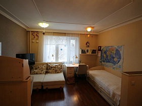 разложенный диван с подушками, деревянная кровать , письменный стол со стулом и навесная полка с книгами в детской комнате семейной трешки