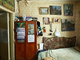 перекидной календарь и фотографии на стеклянных дверцах шкафа, картины на стенах над кроватью в спальне дачи художника времен  СССР