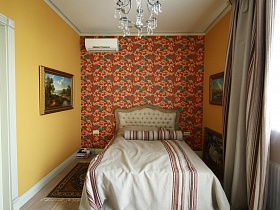 большая деревянная кровать со светлым покрывалом у яркой цветной стены,картины на желтых стенах спальни девчачьей дизайнерской квартиры