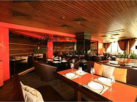 реечный деревянный  потолок с вентиляцией и освещением в зале с ораньжевыми балками и колоннами, двухцветными столиками в уютных зонах евро ресторана