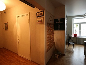 вид из прихожей на белую кухню с комнатным цветком на подоконнике и стульями на полу лофт квартиры художника