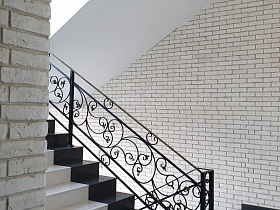 белые кирпичные стены у лестницы с черными фигурными перилами современного стильного подъезда жилого дома