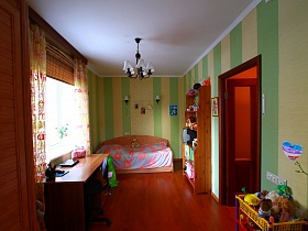 общий вид детской комнаты с деревянной кроватью, открытым шкафом с книгами, телевизором, фотографиями, полкой с игрушками, письменным столом в квартире государственного служащего