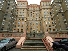 припаркованные машины у лестницы с железными перилами и пандусом к жилому сталинскому дому