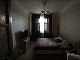 большая подвесная люстра с круглыми плафонами на белом потолке над большой деревянной кроватью спальной комнаты с цветными обоями