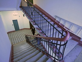 металлическая лестница на ступенях лестничного пролета у белой стены подъезда жилого дома на Новослободской