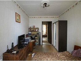 коричневый шкаф с белыми дверцами, зеркалом по центру и этажерка с книгами у входной двери в спальную комнату типичной двухкомнатной квартиры