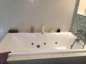 косметические принадлежности на белой джакузи, зашитой квадратной белой плиткой в ванной комнате